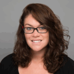 a woman with brown curly hair and glasses smiles at the camera